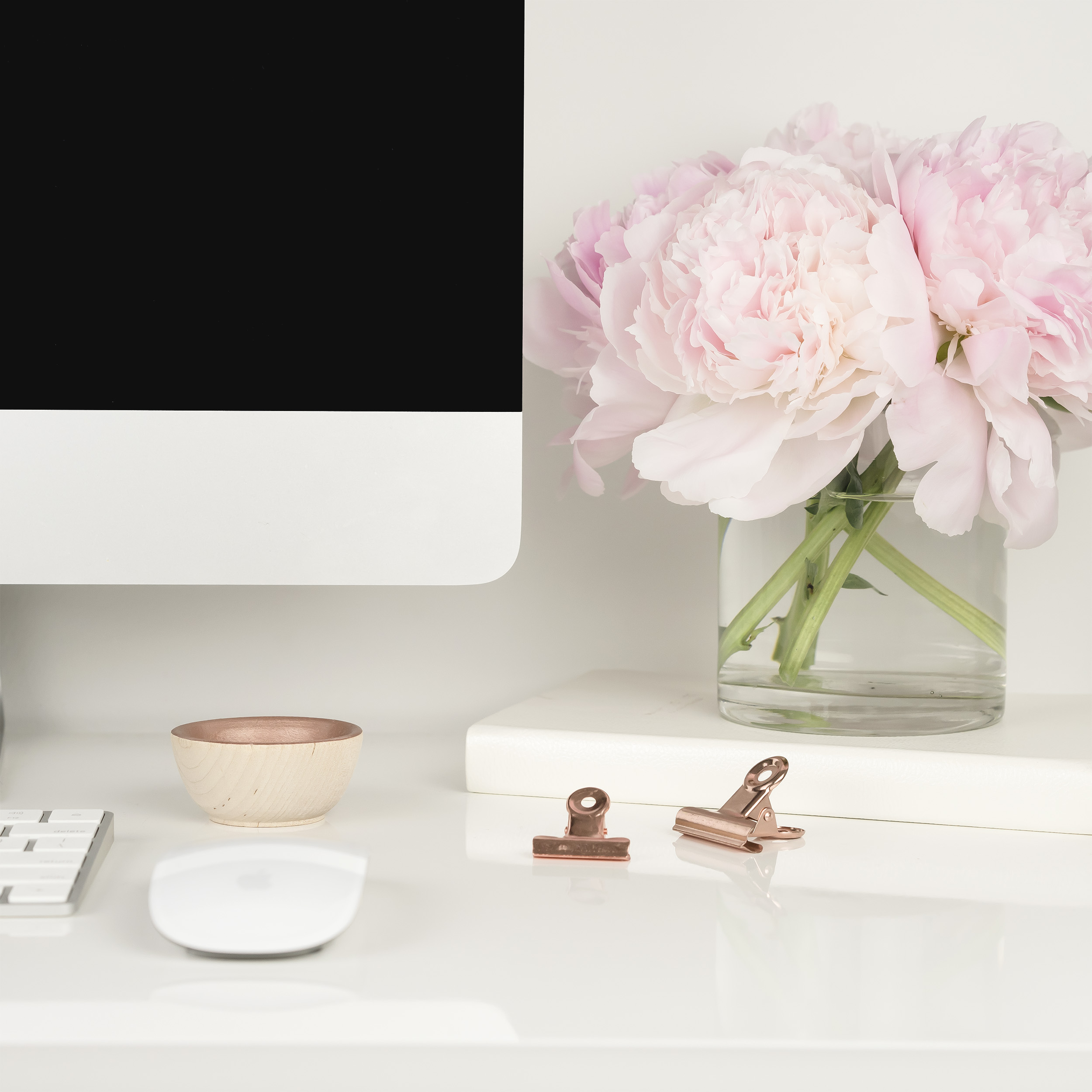 A desktop computer and a vae of pink flowers